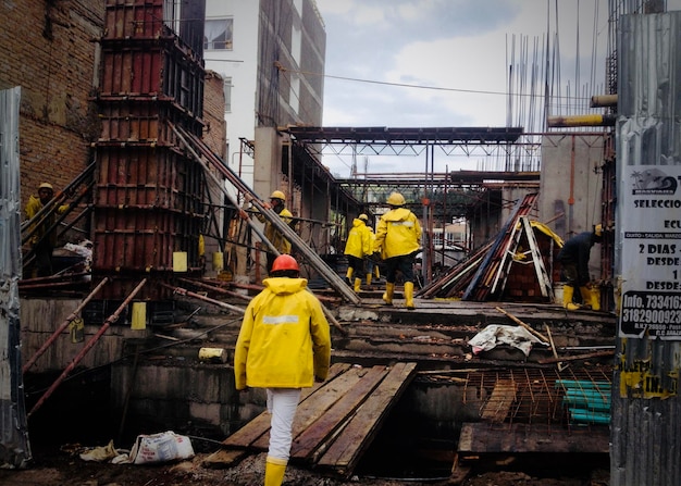 An image of a construction site, where workers can be seen wearing safety gear such as helmets and high-visibility vests, while also being exposed to heavy machinery and potential fall risks.