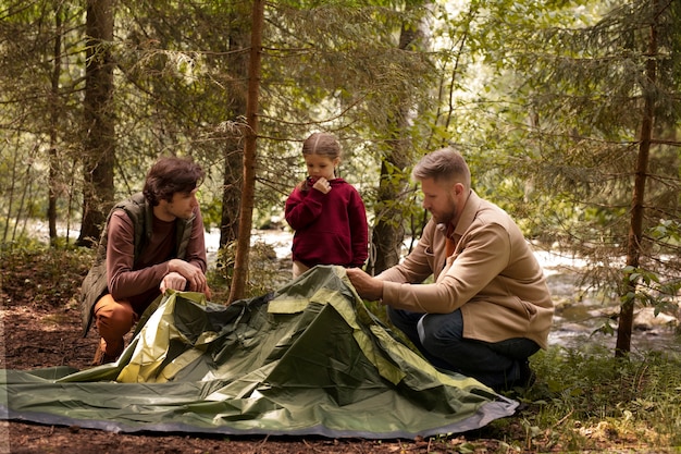 A family setting up a tent at a campsite in a national park, with camping gear neatly arranged around them and a forest backdrop.