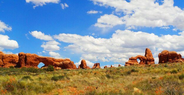 A panoramic view of the Badlands in Theodore Roosevelt National Park, featuring layered rock formations, rolling hills, and sparse vegetation under a clear blue sky.