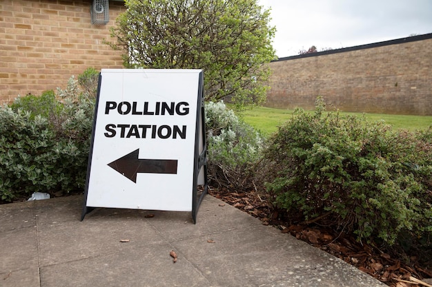 A sign indicating a polling location, with arrows pointing in the direction of the entrance. The sign is placed outside a public building.