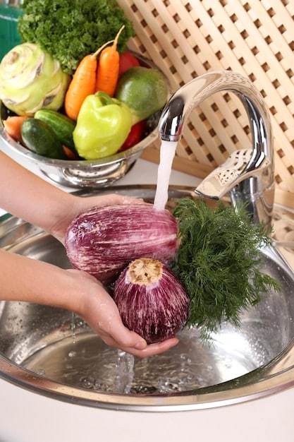 Close-up of hands thoroughly washing raw vegetables under running water in a clean kitchen sink, emphasizing the importance of rinsing produce before consumption.