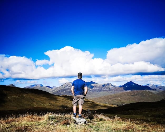 A hiker standing on the grassy summit of Black Balsam Knob, with a vast expanse of rolling mountains in the background. The sky is clear and blue.