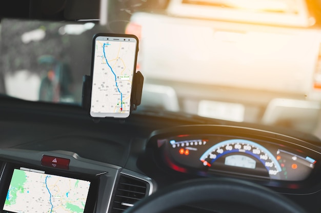 A close-up of a car dashboard with a smartphone mounted for GPS navigation. The phone displays a map with the route highlighted.