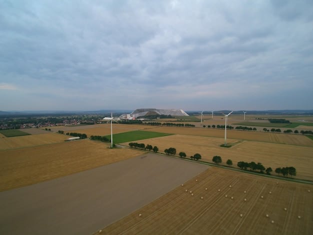 An aerial view of a wind farm in Iowa, with turbines spread across a vast field of corn, under a cloudy sky.